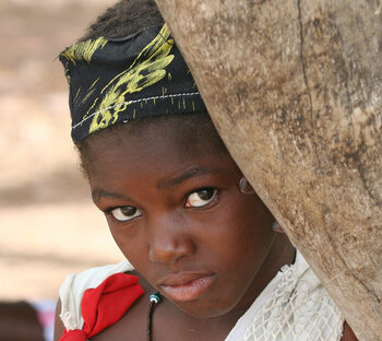 Mädchen aus Mali guckt hinter einem Baum hervor